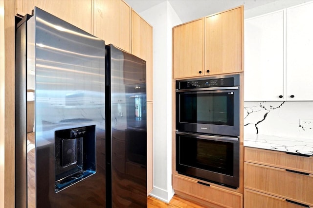 kitchen featuring multiple ovens, stainless steel fridge, decorative backsplash, light stone counters, and light brown cabinets