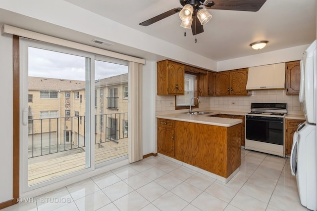 kitchen featuring wall chimney exhaust hood, sink, white gas stove, tasteful backsplash, and kitchen peninsula