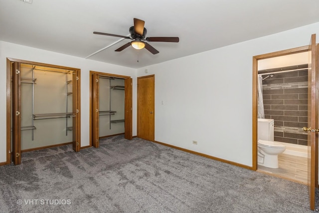 unfurnished bedroom featuring dark colored carpet, connected bathroom, two closets, and ceiling fan