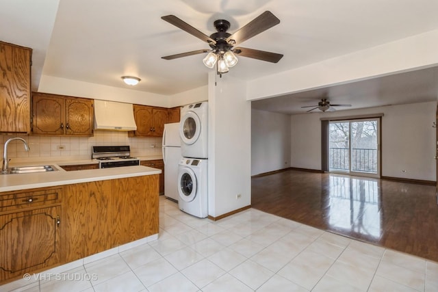 kitchen with sink, kitchen peninsula, white appliances, stacked washer / dryer, and decorative backsplash