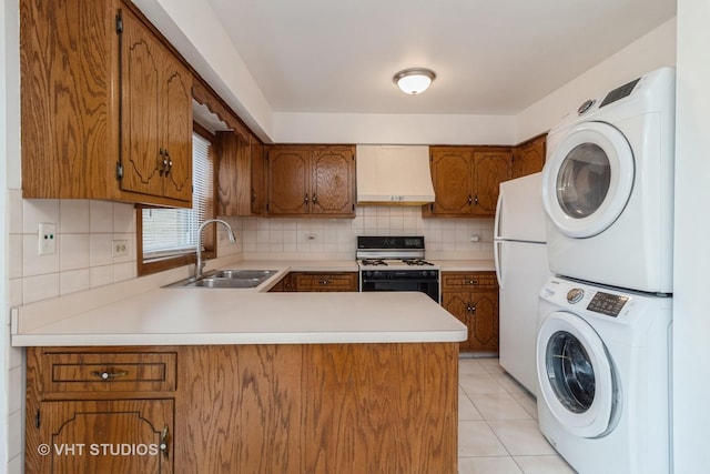 kitchen with sink, stacked washer and clothes dryer, range with gas stovetop, kitchen peninsula, and white fridge