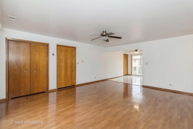 unfurnished bedroom featuring ceiling fan, light hardwood / wood-style floors, and multiple closets