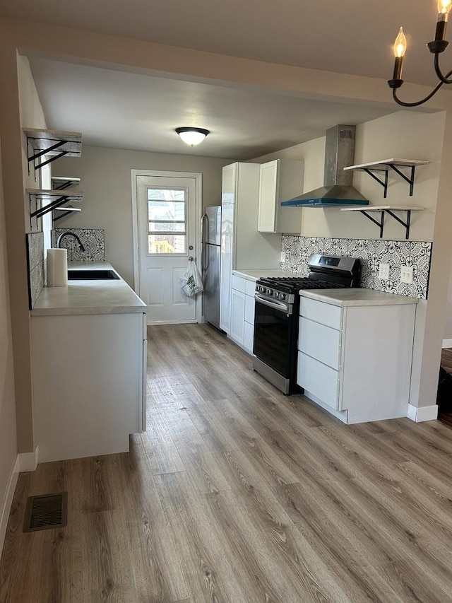 kitchen with sink, appliances with stainless steel finishes, white cabinetry, wall chimney exhaust hood, and light wood-type flooring