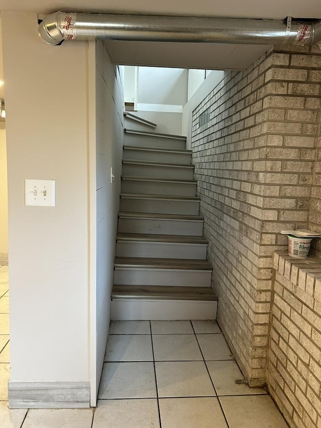 staircase featuring brick wall and tile patterned flooring