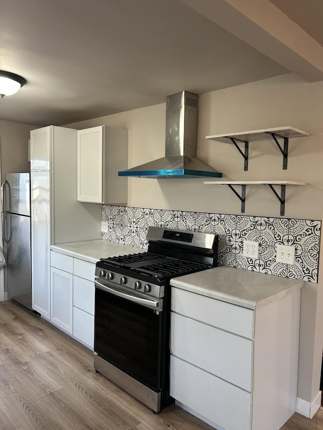 kitchen with white cabinetry, wall chimney range hood, light hardwood / wood-style flooring, and appliances with stainless steel finishes