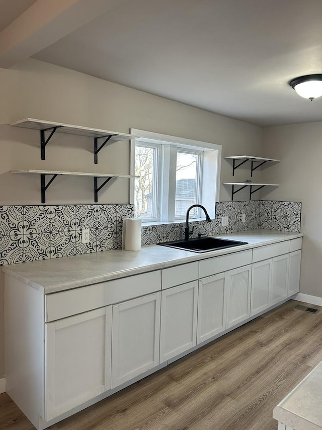 kitchen with tasteful backsplash, white cabinetry, sink, and light hardwood / wood-style floors