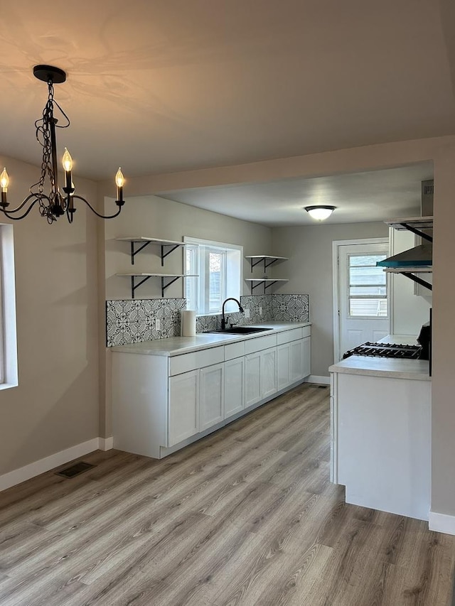 kitchen featuring sink, light hardwood / wood-style flooring, pendant lighting, decorative backsplash, and white cabinets