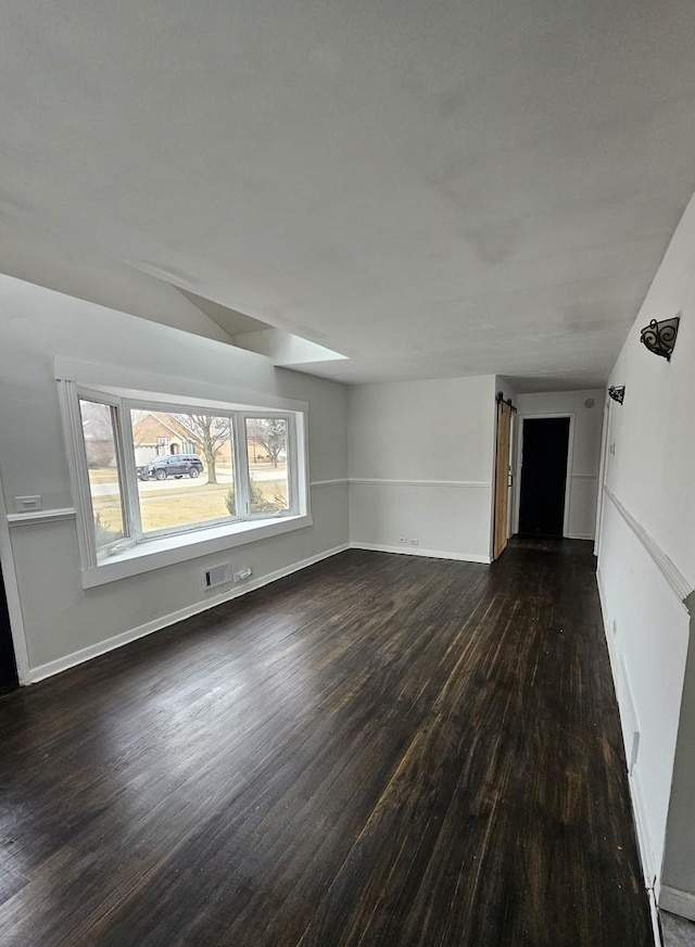 empty room with dark wood-type flooring and a barn door