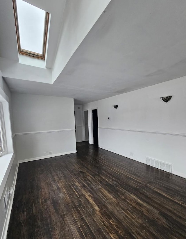 spare room featuring a skylight and dark wood-type flooring