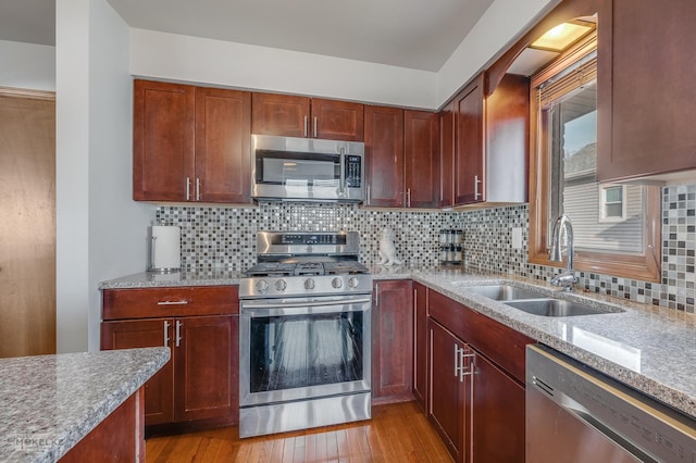 kitchen featuring sink, appliances with stainless steel finishes, backsplash, light stone countertops, and light hardwood / wood-style floors