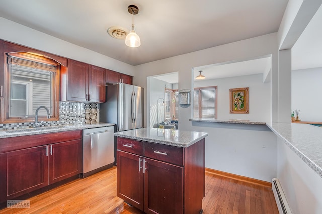 kitchen with appliances with stainless steel finishes, decorative light fixtures, sink, baseboard heating, and light stone countertops