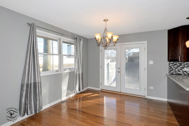 unfurnished dining area featuring an inviting chandelier, wood-type flooring, and french doors