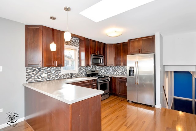 kitchen featuring pendant lighting, appliances with stainless steel finishes, light hardwood / wood-style floors, decorative backsplash, and kitchen peninsula