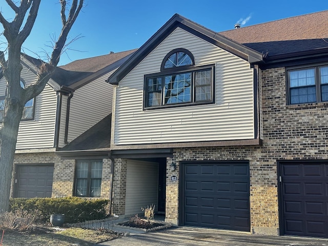 multi unit property featuring a garage, a shingled roof, and brick siding