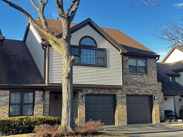 view of front of home with a garage, brick siding, driveway, and roof with shingles