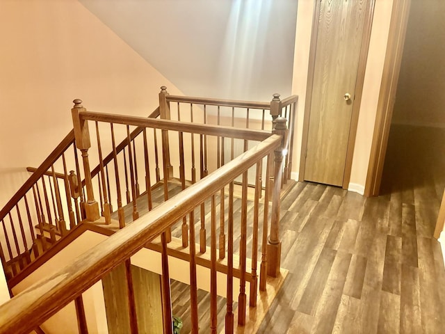 stairway featuring lofted ceiling, baseboards, and wood finished floors