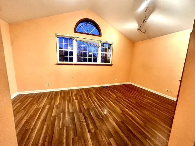 spare room with track lighting, baseboards, vaulted ceiling, and wood finished floors