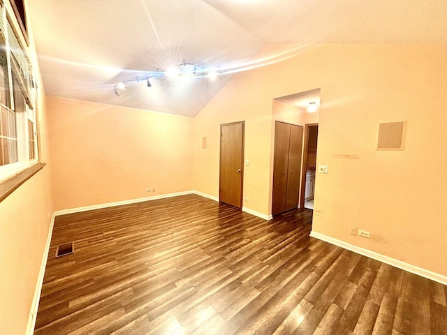 empty room with baseboards, visible vents, lofted ceiling, wood finished floors, and rail lighting