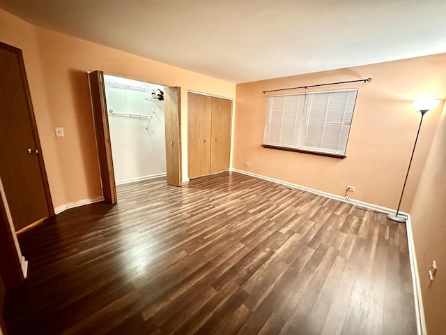 unfurnished bedroom featuring baseboards, dark wood-style flooring, and multiple closets