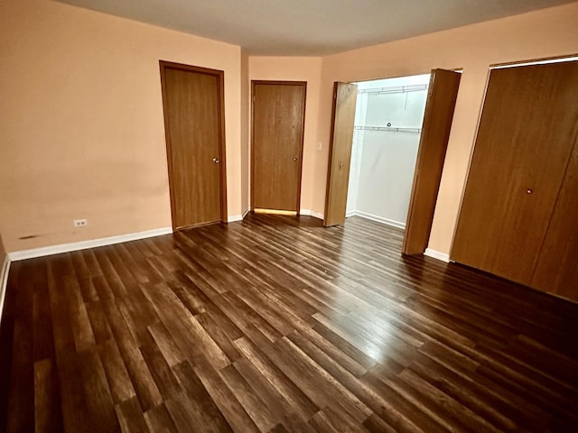 unfurnished bedroom featuring multiple closets, baseboards, and dark wood-type flooring