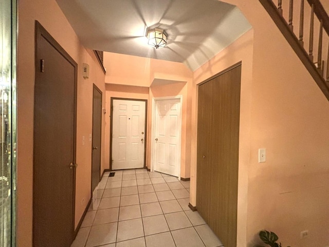 corridor featuring arched walkways, light tile patterned flooring, and baseboards