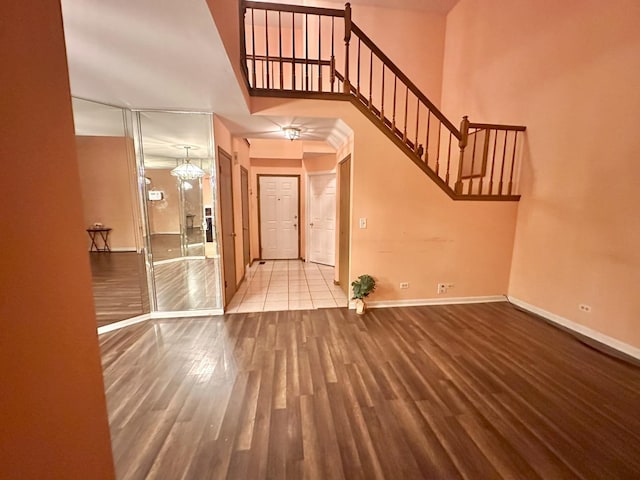 foyer entrance featuring baseboards, a towering ceiling, wood finished floors, an inviting chandelier, and stairs