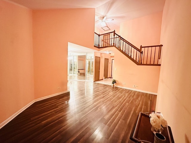 unfurnished living room with a towering ceiling, stairs, baseboards, and wood finished floors