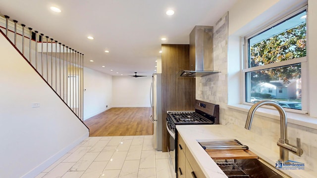 kitchen with wall chimney exhaust hood, sink, ceiling fan, stainless steel appliances, and decorative backsplash