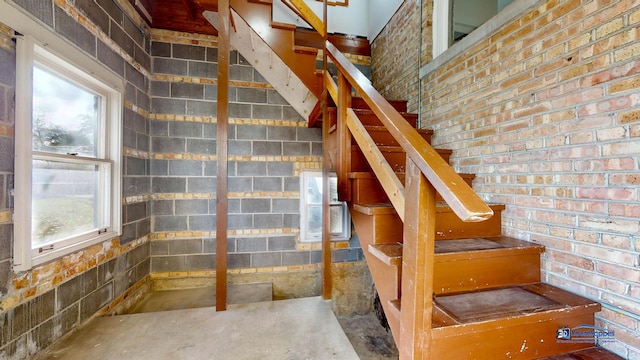 stairs with concrete flooring, brick wall, and plenty of natural light