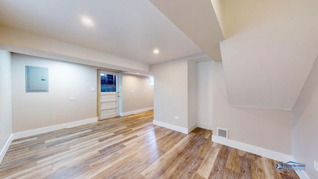 basement featuring electric panel and light hardwood / wood-style flooring