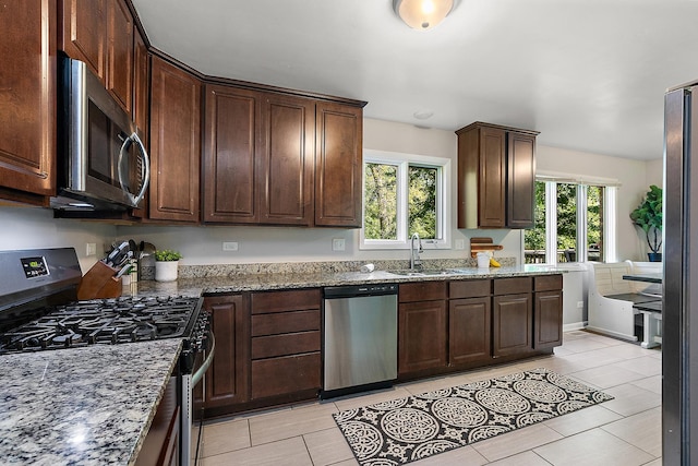 kitchen featuring stainless steel appliances, sink, dark stone countertops, and dark brown cabinetry