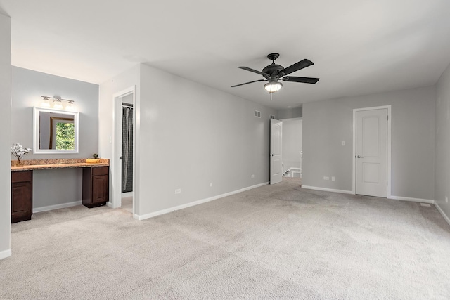 unfurnished bedroom with ceiling fan, connected bathroom, built in desk, and light carpet