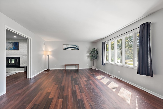 spare room featuring dark hardwood / wood-style flooring and a brick fireplace