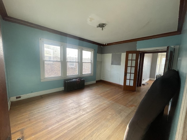 unfurnished living room featuring french doors, ornamental molding, radiator heating unit, and light wood-type flooring