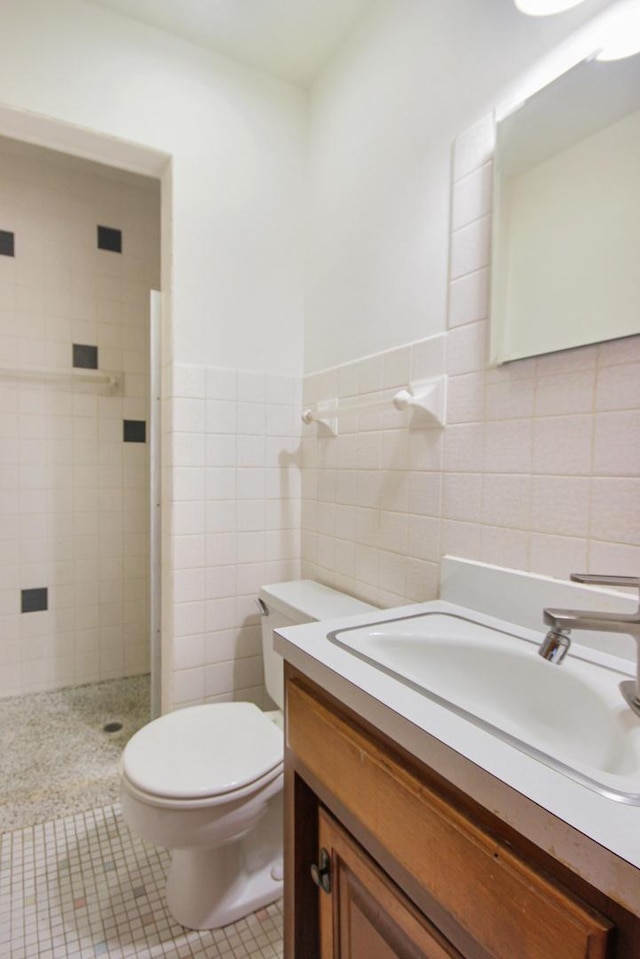 bathroom featuring tiled shower, vanity, toilet, and tile walls