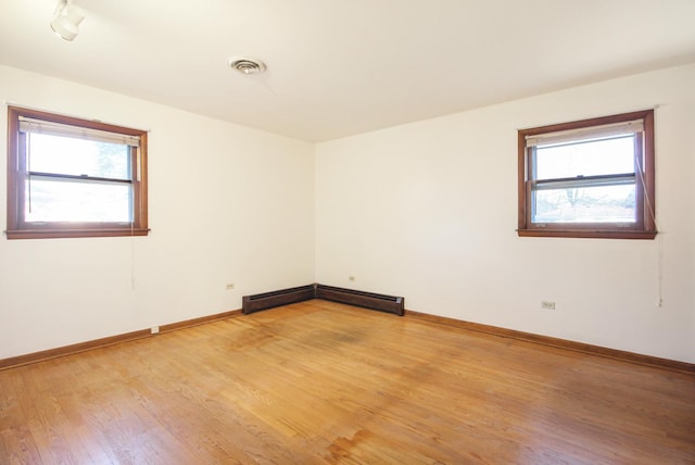 spare room featuring a baseboard heating unit, plenty of natural light, and light hardwood / wood-style floors