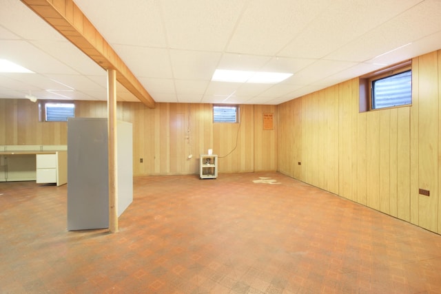 basement featuring a drop ceiling, a healthy amount of sunlight, and wood walls