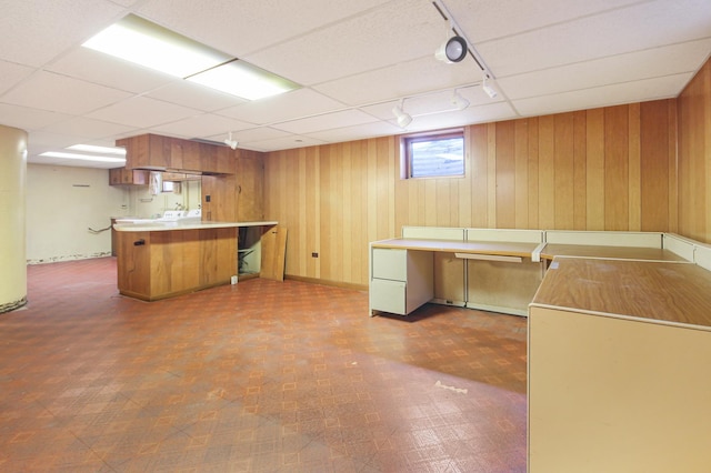 kitchen featuring a paneled ceiling, track lighting, kitchen peninsula, and wood walls