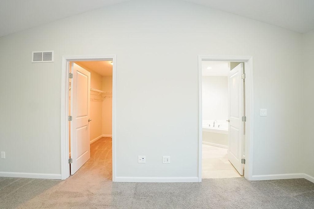 unfurnished bedroom with vaulted ceiling, ensuite bathroom, a walk in closet, light colored carpet, and a closet