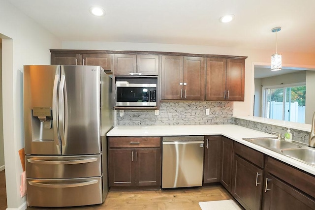 kitchen with sink, backsplash, hanging light fixtures, stainless steel appliances, and light hardwood / wood-style flooring