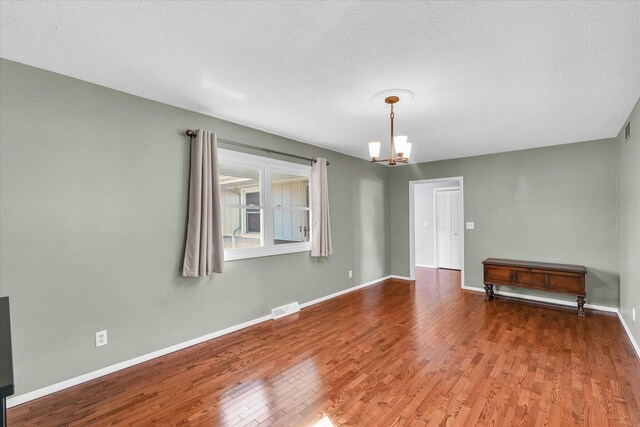 spare room with hardwood / wood-style floors, a notable chandelier, and a textured ceiling