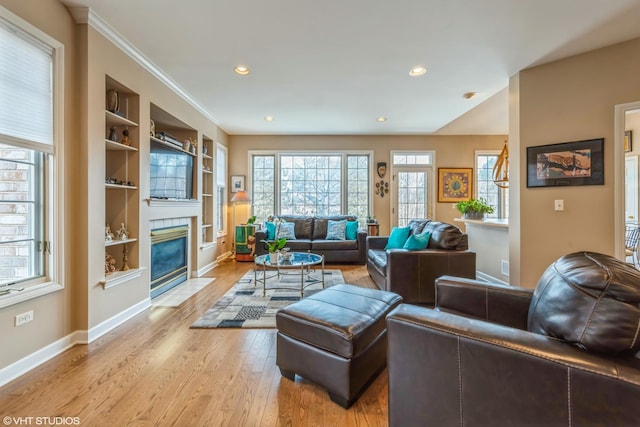 living room featuring ornamental molding, built in features, light hardwood / wood-style floors, and a tile fireplace