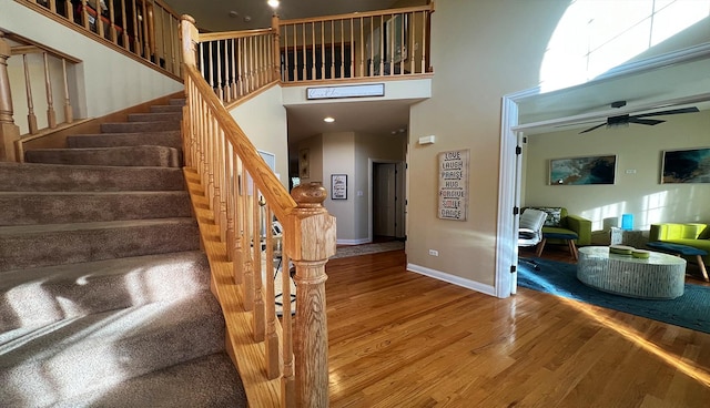 stairs with hardwood / wood-style flooring, a high ceiling, and ceiling fan