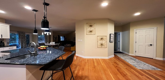 kitchen featuring sink, decorative light fixtures, light wood-type flooring, dark stone countertops, and white cabinets