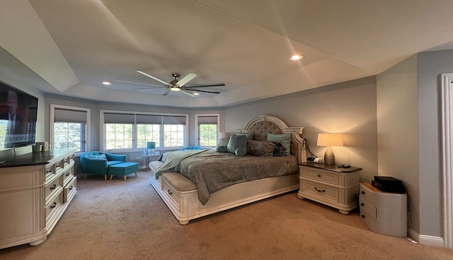 bedroom with a raised ceiling, light colored carpet, and ceiling fan