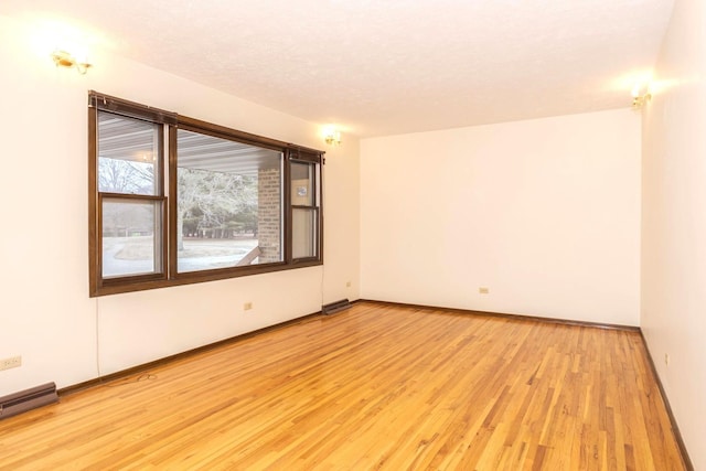 empty room with baseboard heating, a textured ceiling, and light hardwood / wood-style flooring