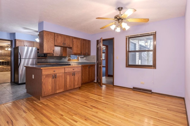 kitchen featuring stainless steel refrigerator, tasteful backsplash, ceiling fan, light hardwood / wood-style floors, and black electric cooktop