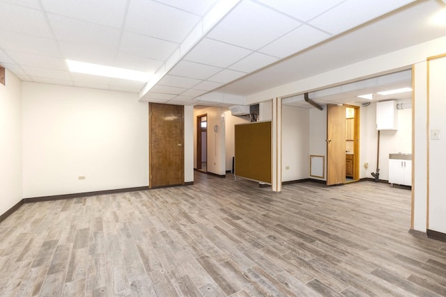 basement featuring wood-type flooring, a drop ceiling, and a wall unit AC