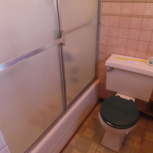 bathroom with shower / bath combination with glass door, toilet, tile patterned flooring, and tile walls