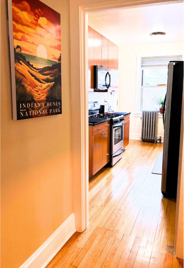 kitchen with appliances with stainless steel finishes, radiator, and light hardwood / wood-style flooring